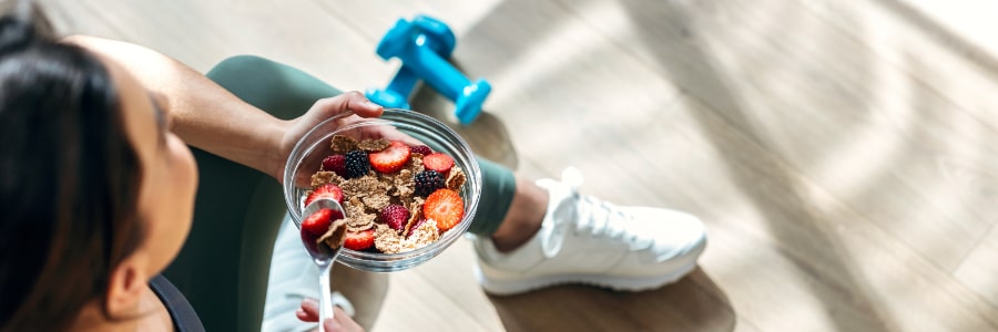 a fit woman eating bowl of cereal and fruit